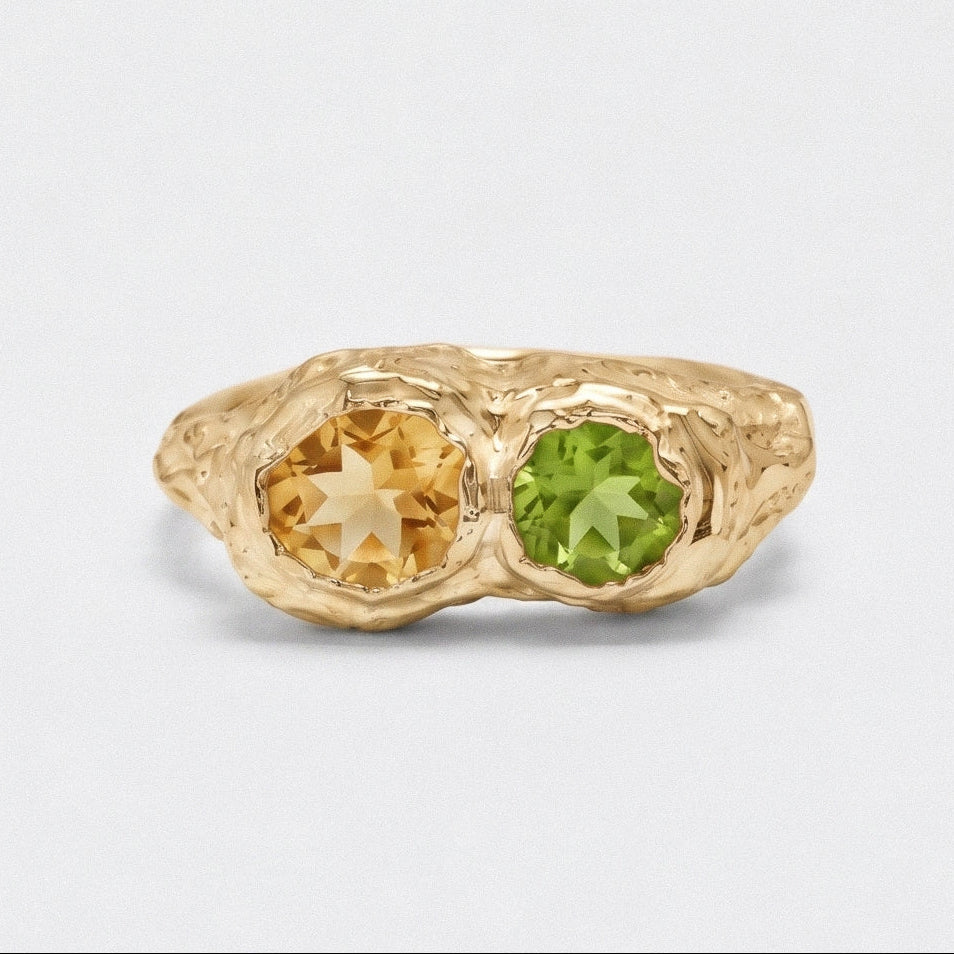 Gold ring with two gemstones, one yellow and one green, on a light gray background