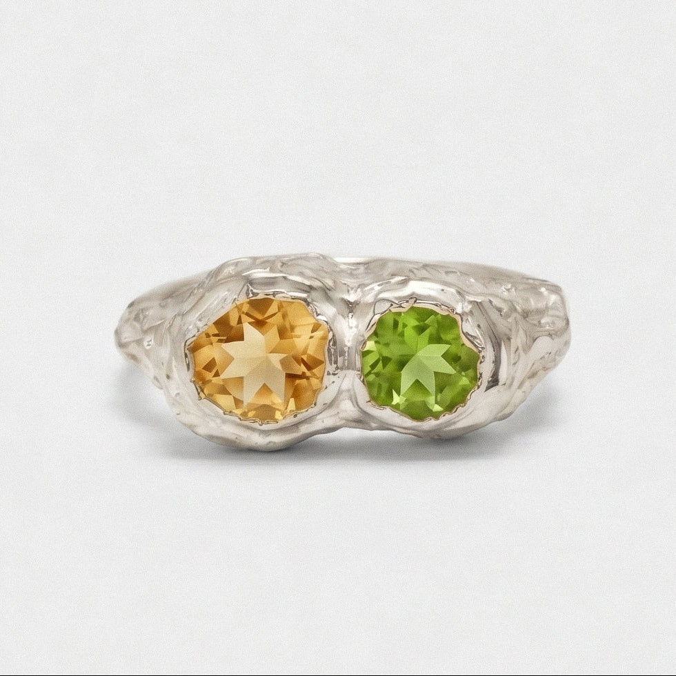 Silver ring with yellow and green gemstones on a light gray background
