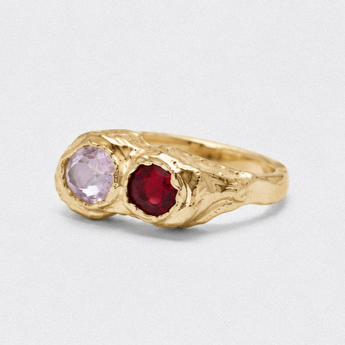 Gold ring with pink and red gemstones on a light gray background