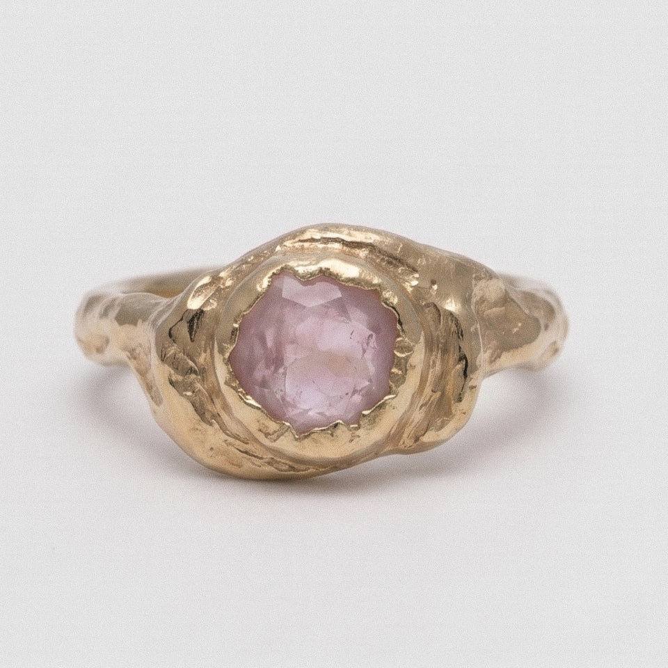 Gold ring with a pink stone on a light gray background