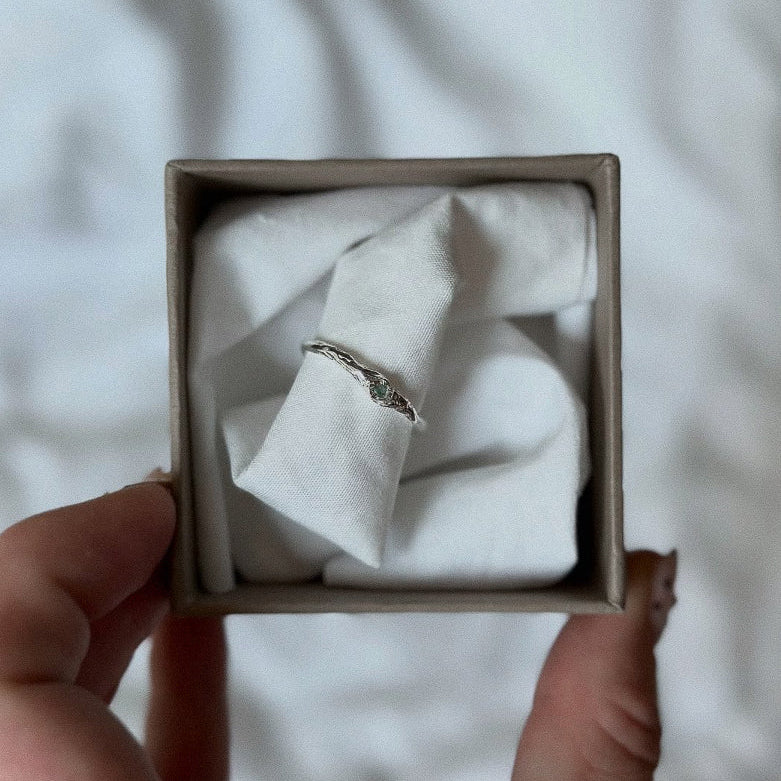 Silver ring with a green gemstone in a box held by a hand on a light background