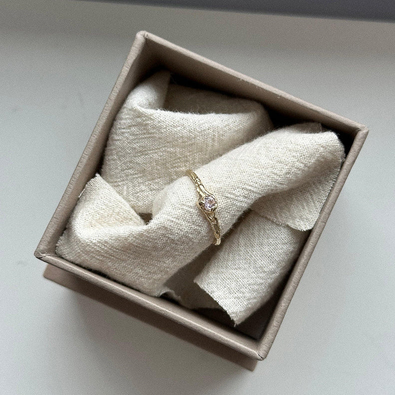 Gold ring with a diamond on soft fabric in a beige box