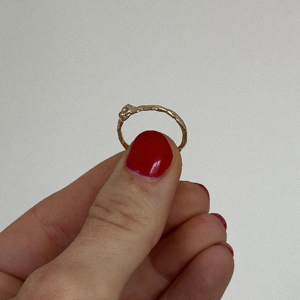 Hand holding a gold ring with a red nail polish on a plain background