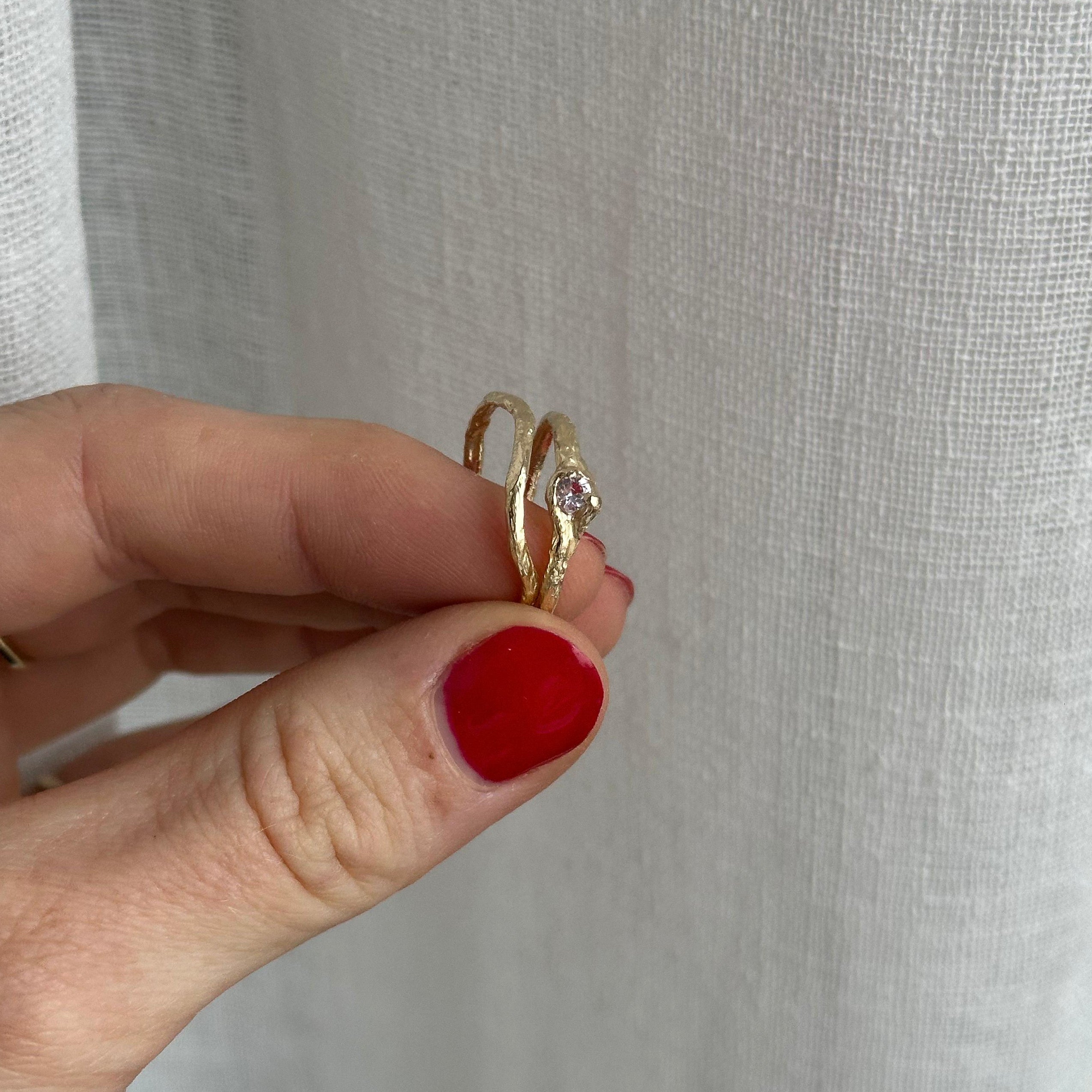 Hand holding a gold ring with a clear stone against a light gray background