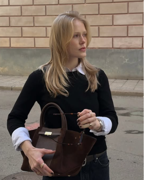 Woman holding a brown handbag on a street with a brick wall background