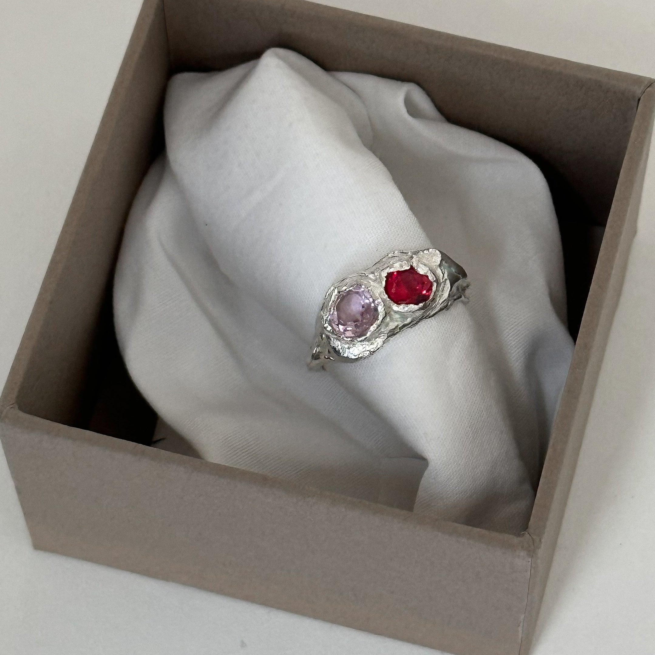 Silver ring with red and pink gemstones in a brown box