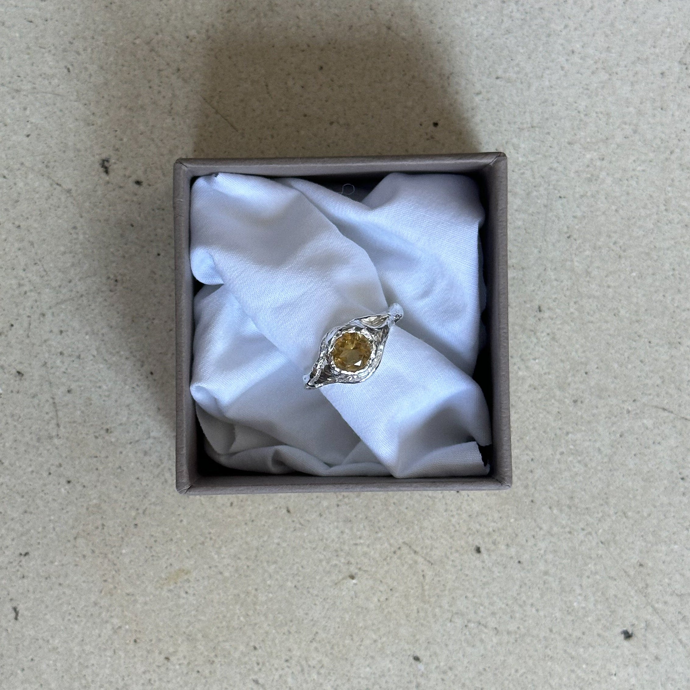 Ring with a yellow gemstone in a box on a patterned surface