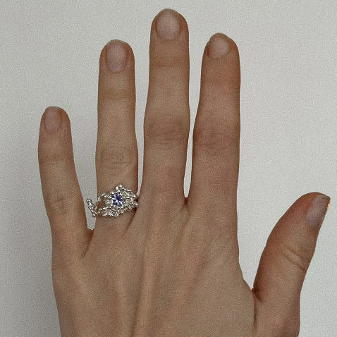 Hand wearing a silver ring with a blue gemstone on a plain background