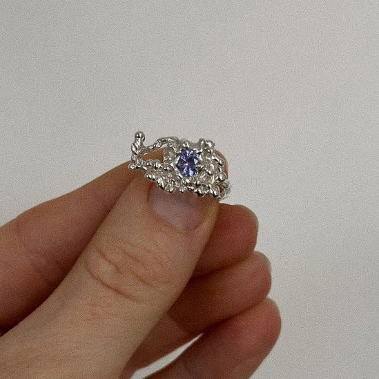 Silver ring with a purple gemstone held between fingers against a plain background